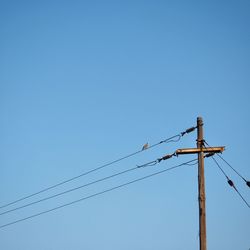 Low angle view of telephone pole against clear blue sky