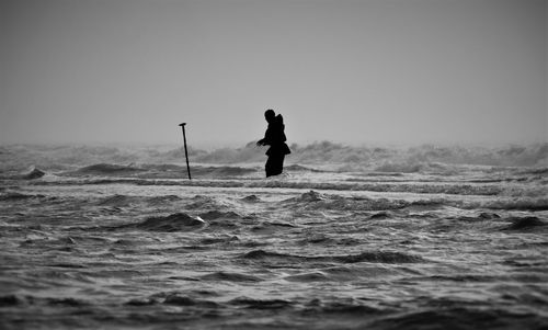 Silhouette man standing in sea against clear sky