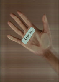 Cropped hand holding paper with text on window