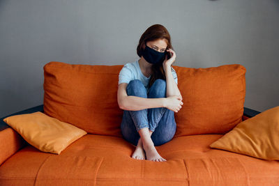 Young woman using phone while sitting on sofa at home