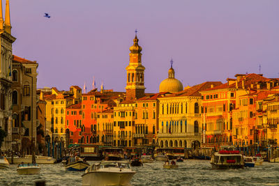 Boats in canal amidst buildings against sky during sunset