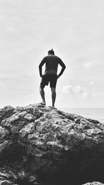 Rear view of man standing on rock at shore against sky