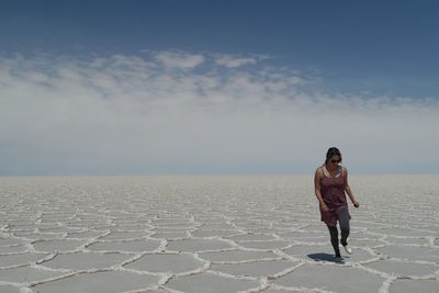 Woman walking on salt desert against cloudy sky