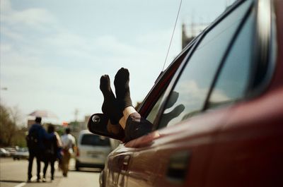 Low section of person relaxing in car on road against sky