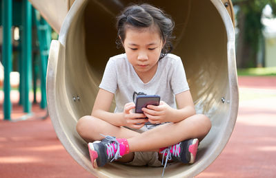 Girl using mobile phone while sitting on slide 