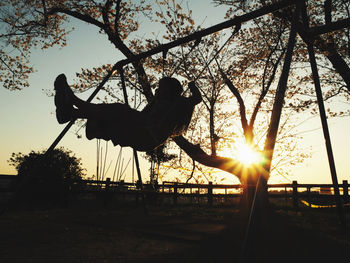 Silhouette man playing at playground against sky during sunset
