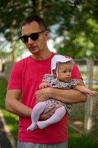 Portrait of young woman wearing sunglasses standing against trees