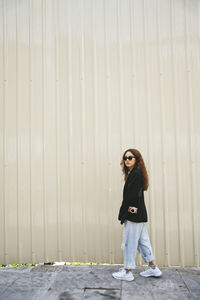 Full length portrait of woman standing against wall