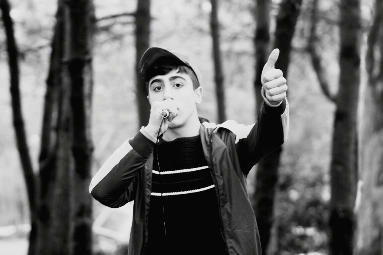 focus on foreground, lifestyles, casual clothing, standing, leisure activity, waist up, front view, person, three quarter length, young adult, looking at camera, portrait, holding, smiling, tree, happiness, jacket, day