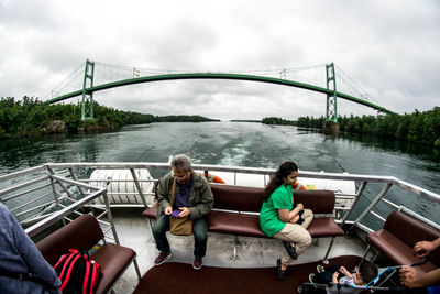 People sitting on bridge over river against sky