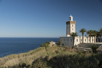 Lighthouse by sea against clear sky