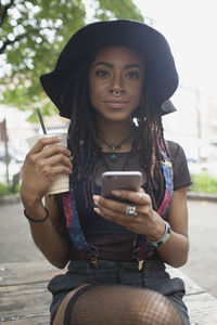 A young woman on her cell phone whilst holding an iced coffee.
