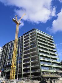 Low angle view of a yellow crane on the construction site of a building set agai st blue sky. 