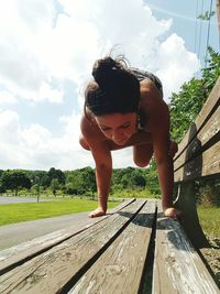 Full length of woman performing yoga on wooden bench against sky