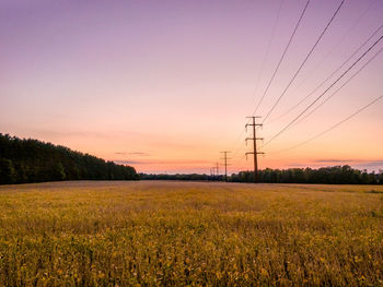 Power lines on field against sky during sunset