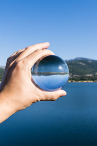 Midsection of person holding ball against blue sky
