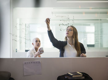 Woman writing on window while working with colleague in office