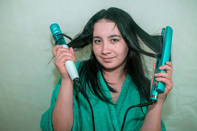 Close-up portrait of young woman holding curling tongs and hair straightener