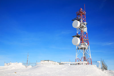 Low angle view of communication tower on snow field against blue sky