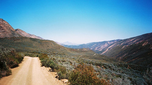 Country road leading towards mountains against blue sky