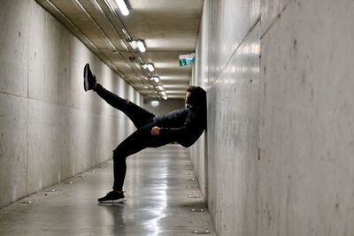 Side view of boy raising leg in a corridor 