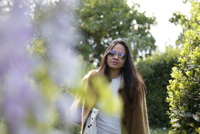 Young woman wearing sunglasses standing against plants