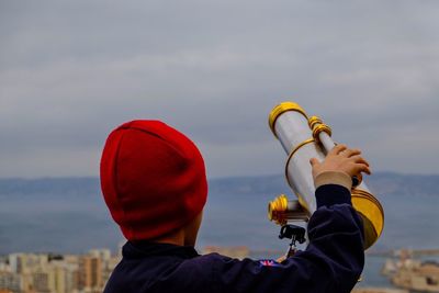 Rear view of boy holding telescope against sky