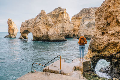 Rear view of woman standing on rock by sea