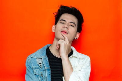 Portrait of young man looking away against orange background