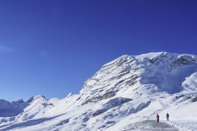 Man and woman walking on snowcapped mountains against blue sky during sunny day