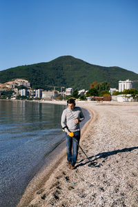 Rear view of man standing at beach against clear blue sky