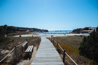Boardwalk on beach against clear blue sky