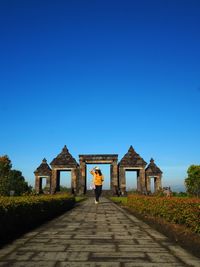 Rear view of woman standing outside house against clear blue sky