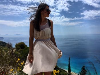 Young woman standing by sea against sky