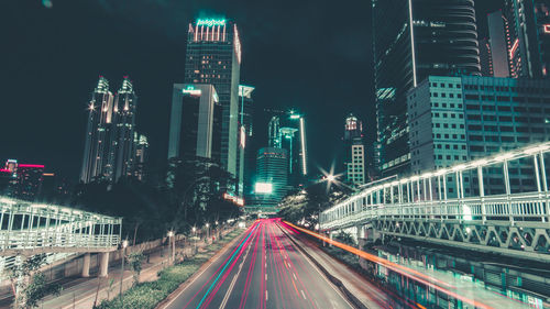 Light trails on road amidst illuminated buildings in city at night
