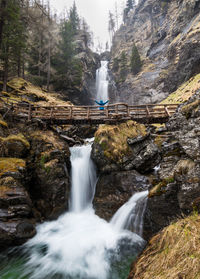 Low angle view of person standing on footbridge against waterfall