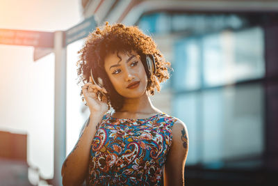 Fashionable young woman with curly hair listening music in city