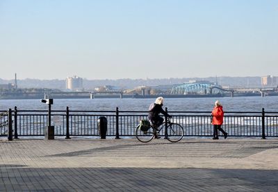 People on bridge over river in city against clear sky