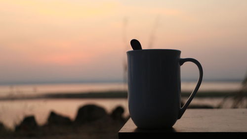 Close-up of coffee cup on table against sky during sunset