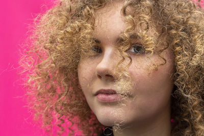 Portrait of beautiful cheerful curly girl on bright pink background, blonde caucasian woman 