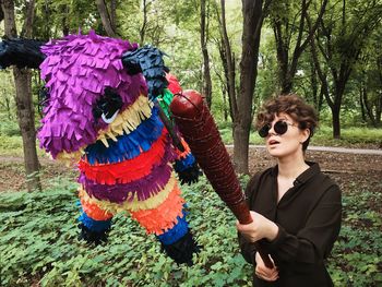 Woman holding toy while standing against trees in forest