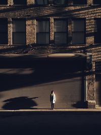 Mid distant view of woman standing on footpath against building