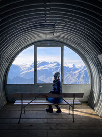 Woman sitting on seat against sky seen through window