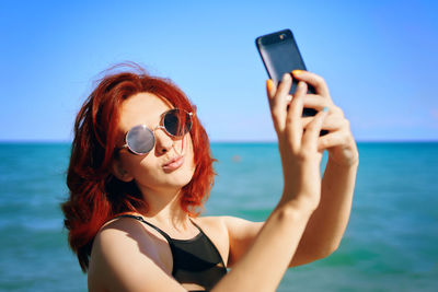 Portrait of young woman using mobile phone against sea