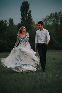 Cheerful couple walking on grass against sky