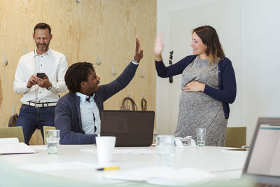 Happy multi-ethnic coworkers giving high-five to each other at conference table