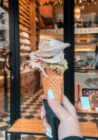 Close-up of hand holding ice cream cone. blurred background of the shop and bokeh of daytime light.