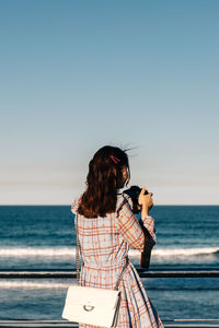 Side view of woman photographing sea against clear sky