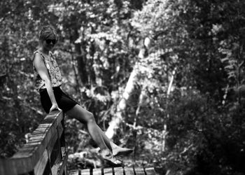 Portrait of woman sitting on railing against trees