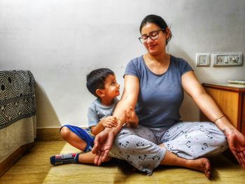 Mother meditating while sitting on floor with boy against wall at home